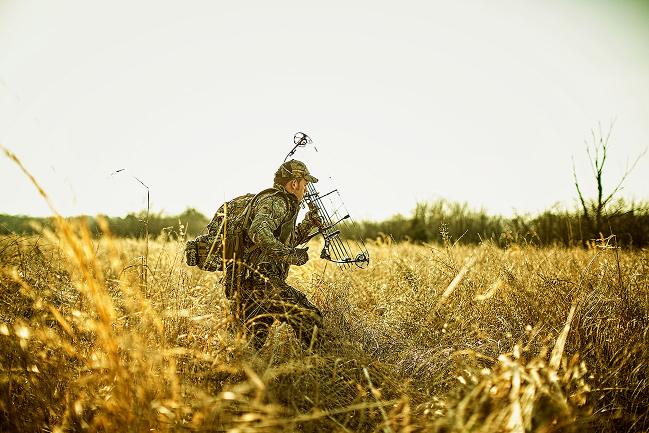 hunter walking through a field with a crossbow